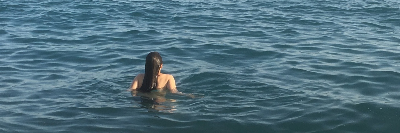 How I Felt Like Myself Again After Treatments for Lyme Disease A woman swimming in the ocean, looking at some ships in the distance.