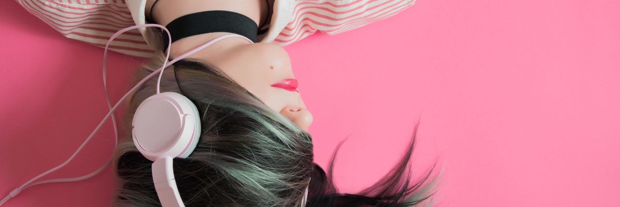 How Music Affects Me as Someone With Borderline Personality Disorder girl with hair covering face on pink background listening to music in headphones