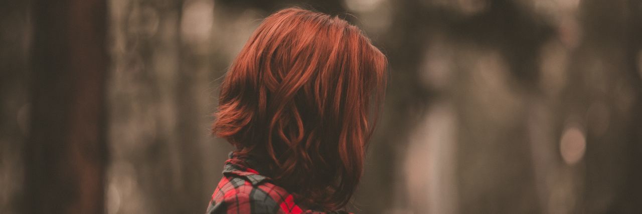 Why We Need to Talk About Premenstrual Dysphoric Disorder woman with red hair stands in the forest