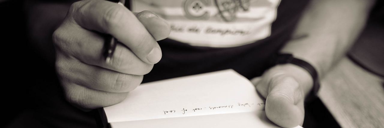 black and white close up of man writing in notepad