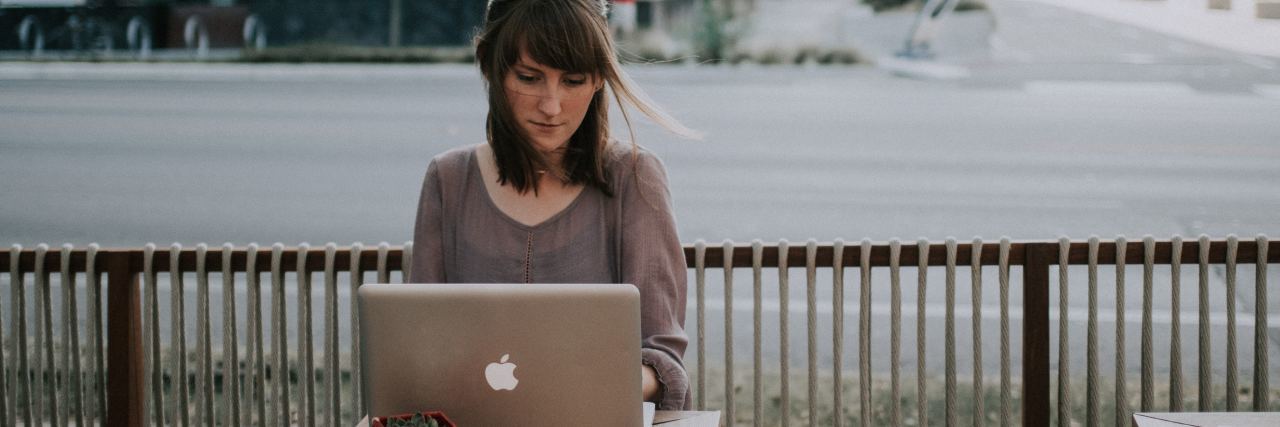 What It's Like to Be a Blogger Struggling With Anxiety woman sitting outside at a cafe on her computer