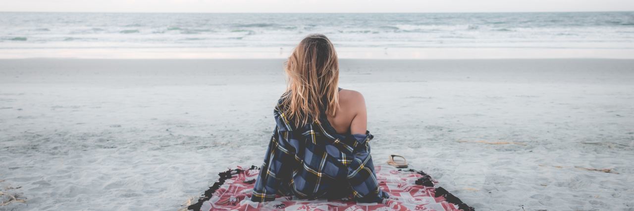 woman sitting on a blanket on the beach looking at the ocean