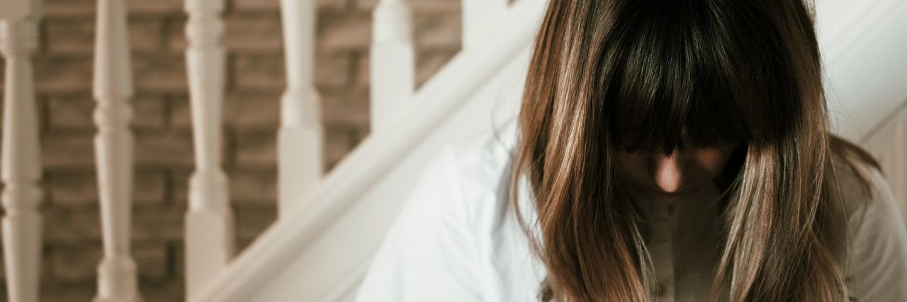 a woman standing by a staircase with brown hair looks down