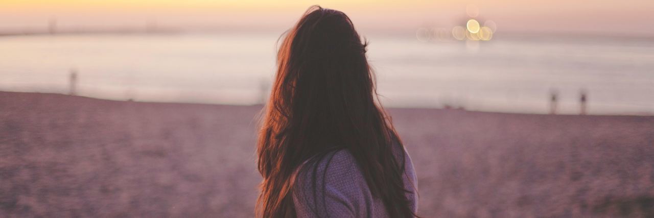 Am I Deserving of Mental Health Care? woman standing on a beach looking at sunset