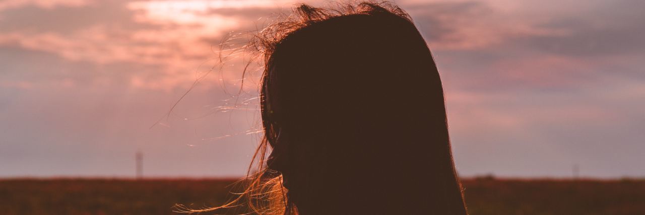 The Beautiful Lesson Loss Taught Me About Manic Depression a woman's sillhoutte stand in front of a beautiful pink sky