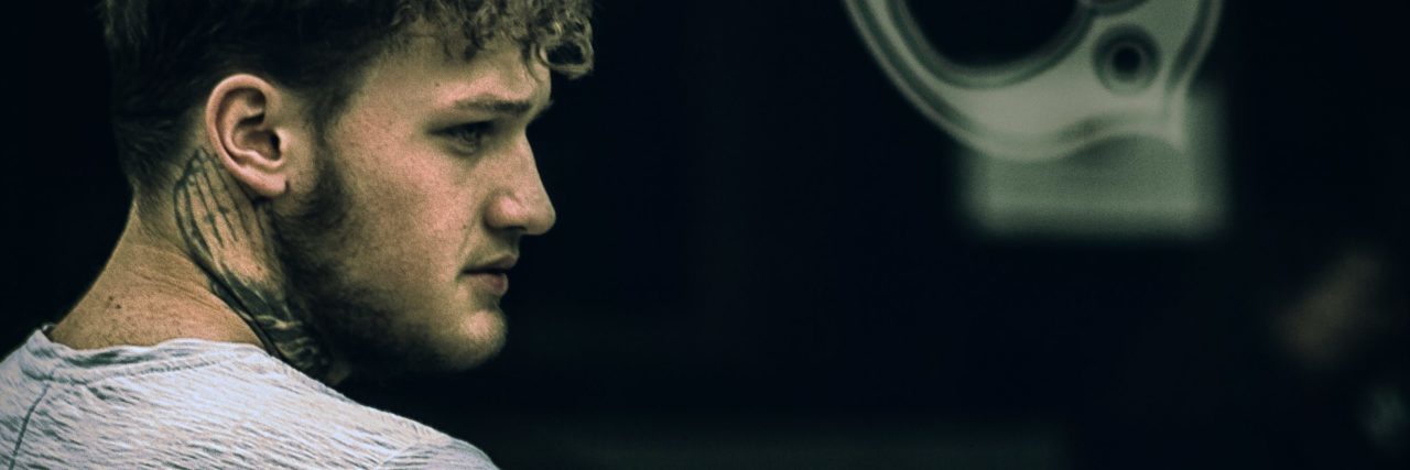 What It’s Like to Be a Guy With Bulimia man standing in profile in dark area with graffiti on walls hugging his arm and looking upset