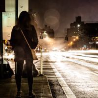 A woman stands on the side of a street at night with traffic lights all around her