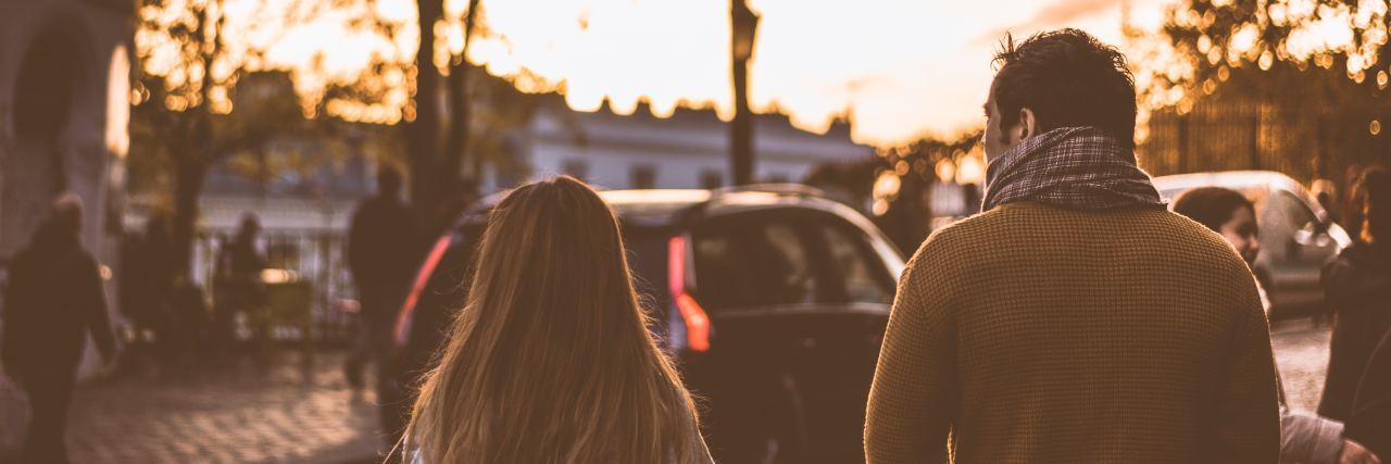 a father and daughter walk along a street in the fall