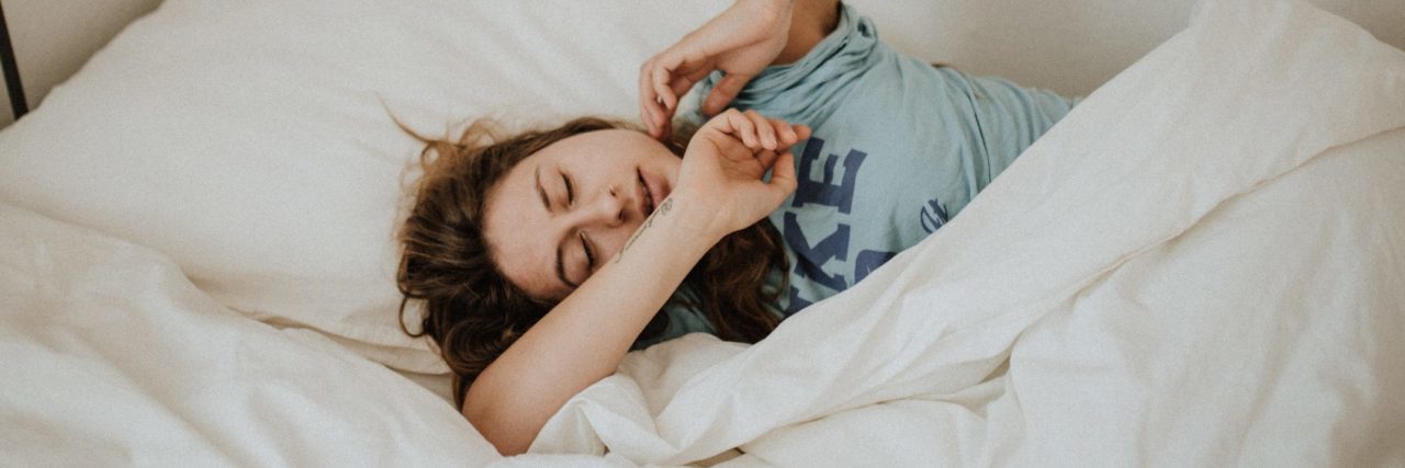 Why I'm Afraid of Taking a Mental Health Day young woman lying in bed stretching