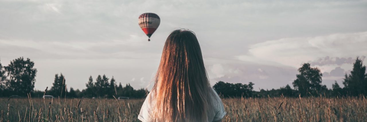 young woman standing in field watching hot air balloons in distance