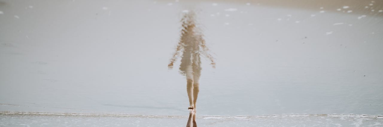 a woman sees her reflection in the sea in front of her