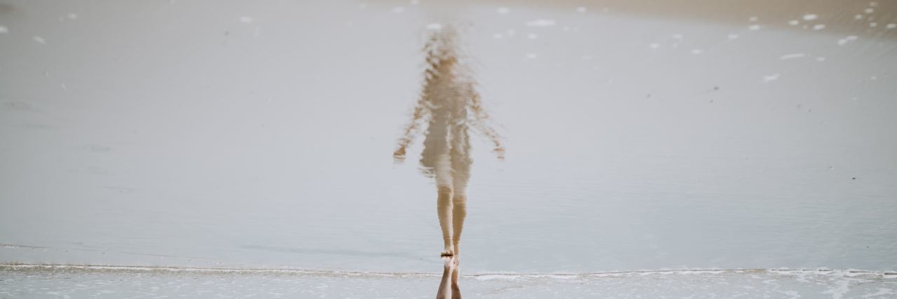 How Depression Turned Me Into Someone I'm Not a woman sees her reflection in the sea in front of her