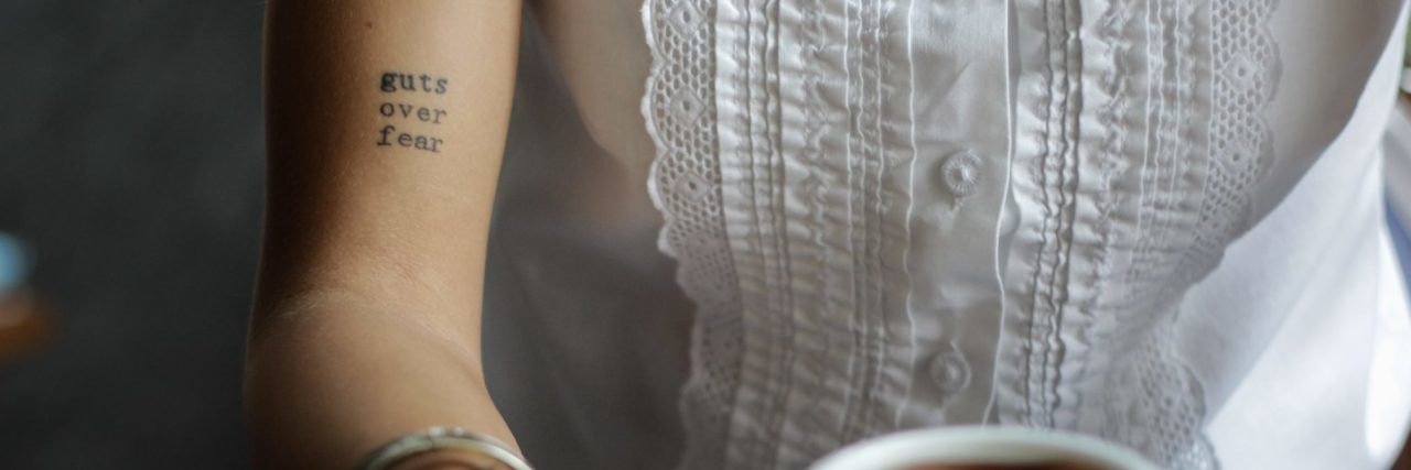 Why We Need to Talk About the Truth of OCD woman holding coffee cup with tattoo saying guts over fear