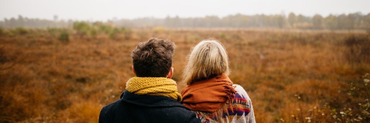 couple standing side by side looking across misty field