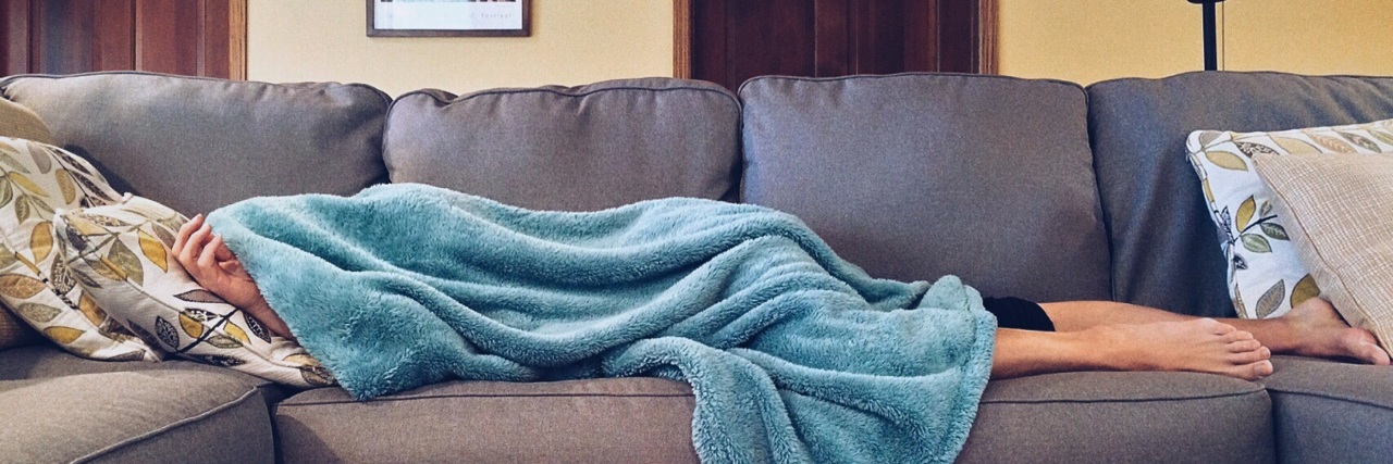 woman laying on couch under blanket