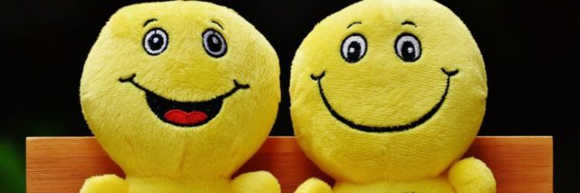 two smiley face stuffed toys sitting on a bench