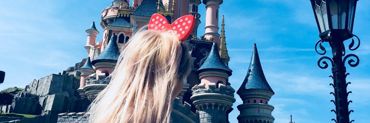 young blonde woman at disneyland looking at magic kingdom castle