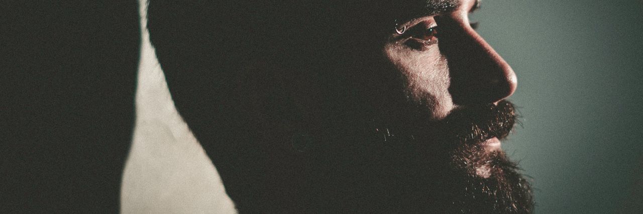 What My Beard Says About My Depression man in dull room with beard and eyebrow piercing leaning against wall looking sad