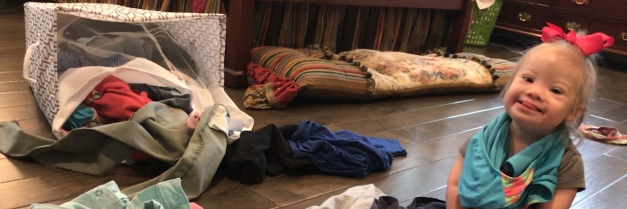 A Letter to My Sweet Little Lady Who Has Down Syndrome Little girl with Down syndrome sitting on the floor in the middle of a pile of dirty laundry