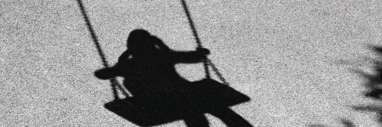 A shadow on concrete of a dissociating child alone on a swing.