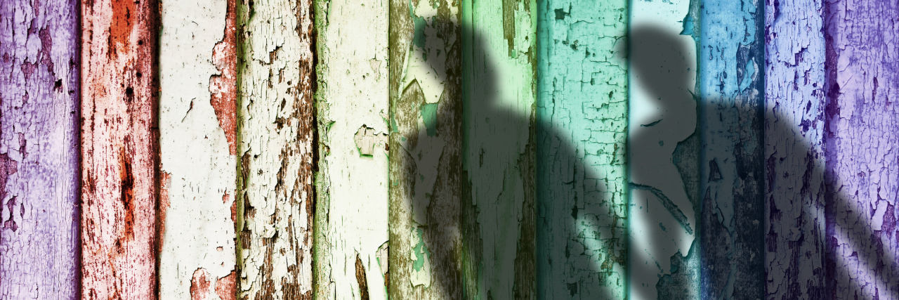 Shadow of two gay men on a rainbow weathered fence.