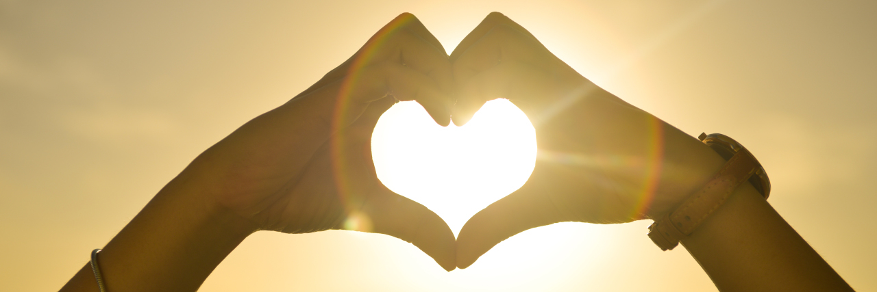 The Importance of the Green Heart Emoji in the Lyme Disease Community hands making a heart in front of a sunrise over the ocean
