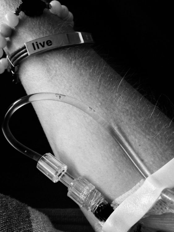 black and white photo of a woman's arm with a bracelet that says 'live' and an IV in her arm