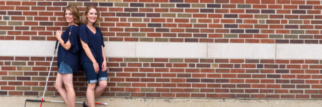 My First Time Using a White Cane to Navigate With Low Vision Jenelle with her twin sister, both standing against a brick wall with their matching canes.