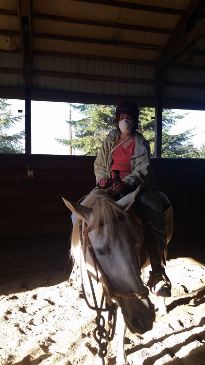 woman sitting on a horse and wearing a face mask