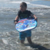 The author's son, holding a boogie board while in the ocean near the shore
