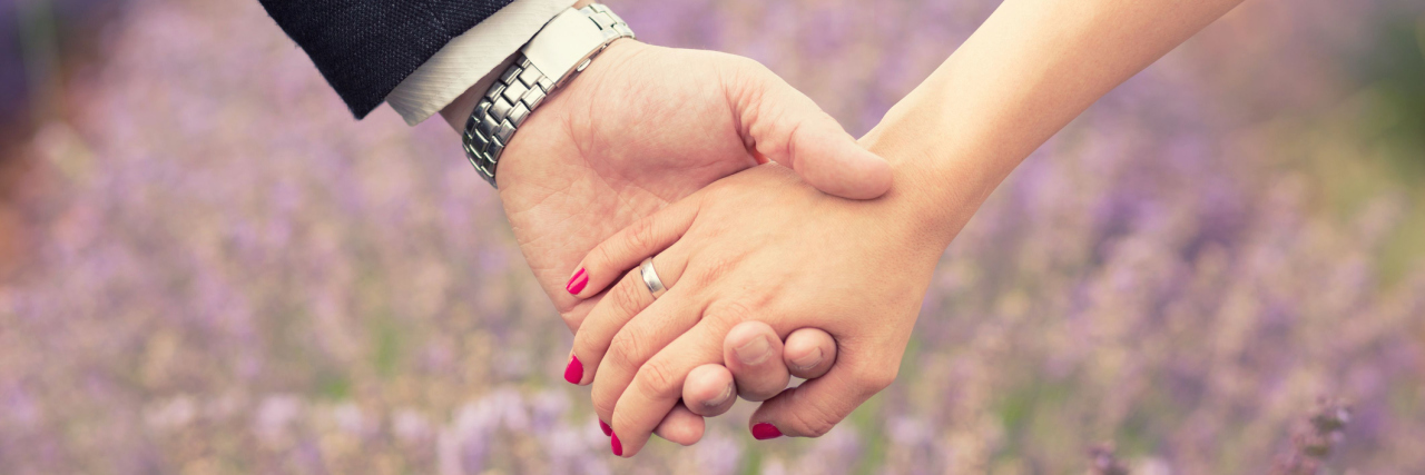 husband and wife holding hands in front of a field of flowers