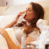 woman blowing her nose while sick in bed