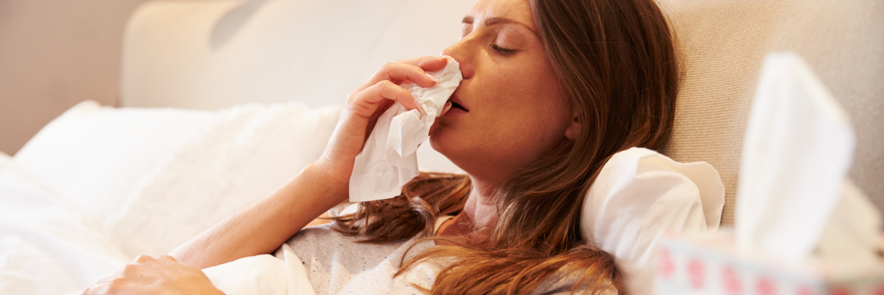 woman blowing her nose while sick in bed