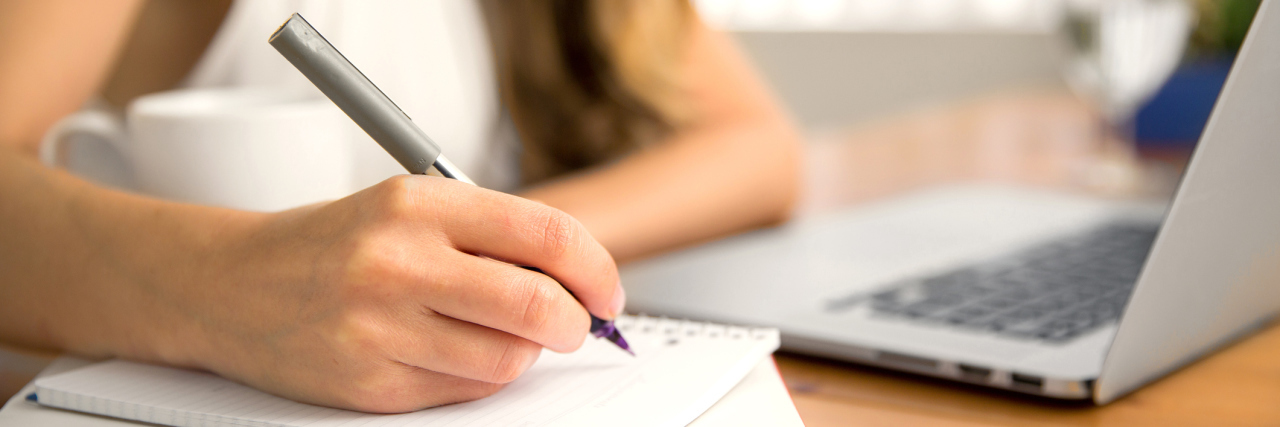 Tips for Staying Organized and Working With a Chronic Illness woman writing on a notepad at her desk at work