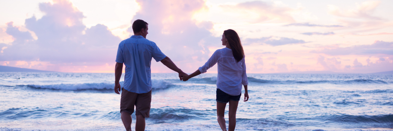 couple holding hands and walking on the beach at sunset