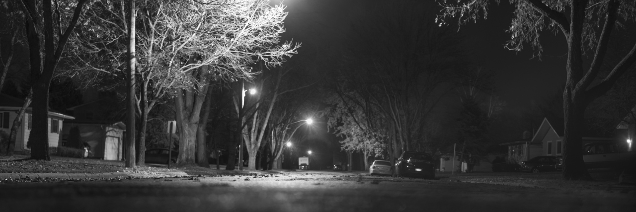 To People Who Aren't Celebrating Halloween Black and white photograph of street in the United States, with lights illuminating parts of it. Taken at night.
