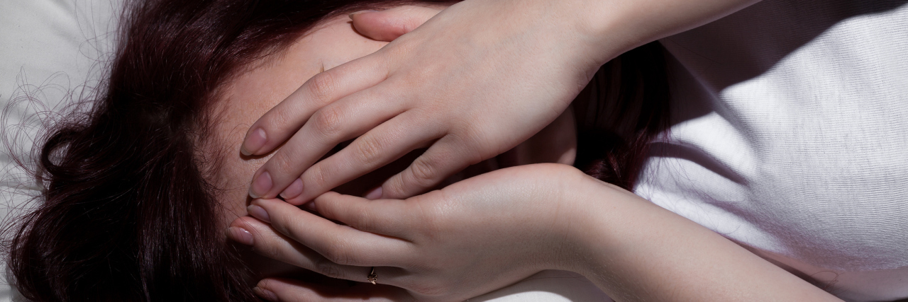 When a Fibromyalgia Flare-Up Triggered Migraines woman lying in bed with her hands covering her face