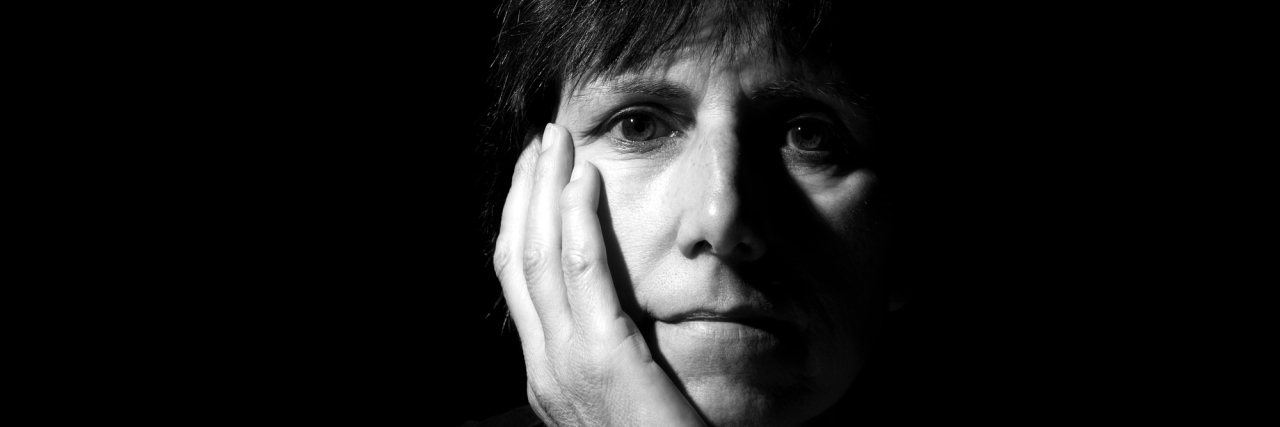 When People Won't Let Me Help Them Because of My Illness A middle-aged woman in the dark, with a shadow going across half of her face.