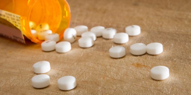 How the Opioid Crisis Complicates Chronic Pain White pills spilling onto a wooden table.