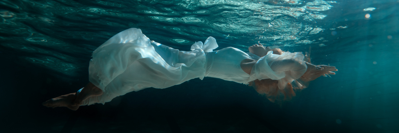 Woman in white dress swimming under water in the pool.