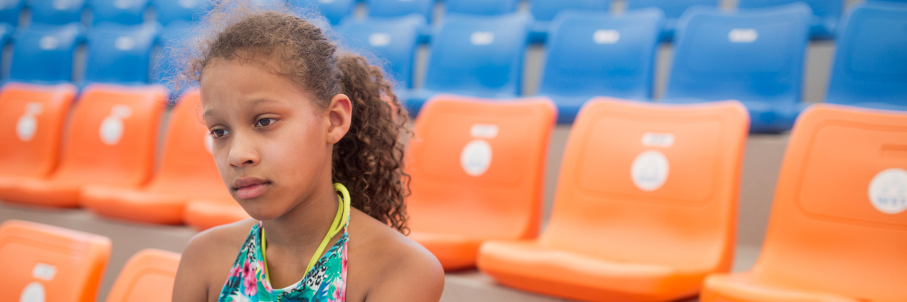 7 Signs You Probably Had Anxiety as a Child Depressed African American teenager sitting on a stadium and watching her favorite sports team loosing a game.