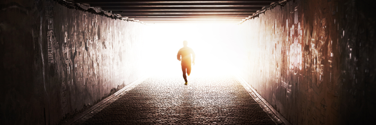 person running through a dark tunnel toward the sun