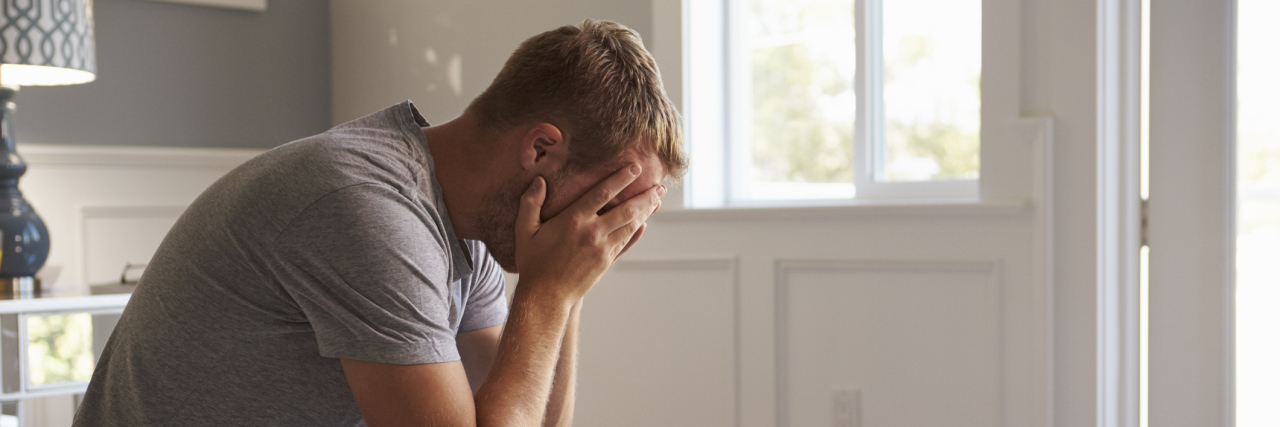 Anxiety and Autism -- Coping Strategies Man sitting on bed with head in hands.
