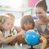 Teacher looking at schoolchildren touching globe.