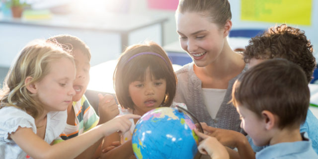 Teacher looking at schoolchildren touching globe.
