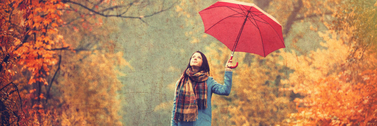A young woman with a red umbrella walking through a park in the fall.