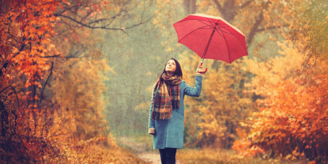 A young woman with a red umbrella walking through a park in the fall.