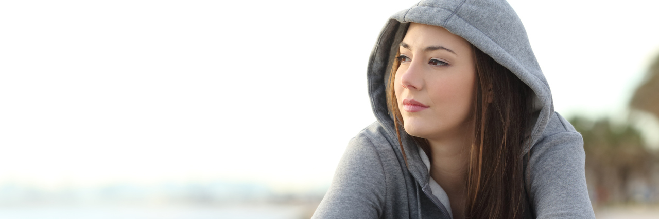 woman in a gray hoodie sitting near the beach looking into the distance