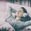 Woman listening to headphones in bed.