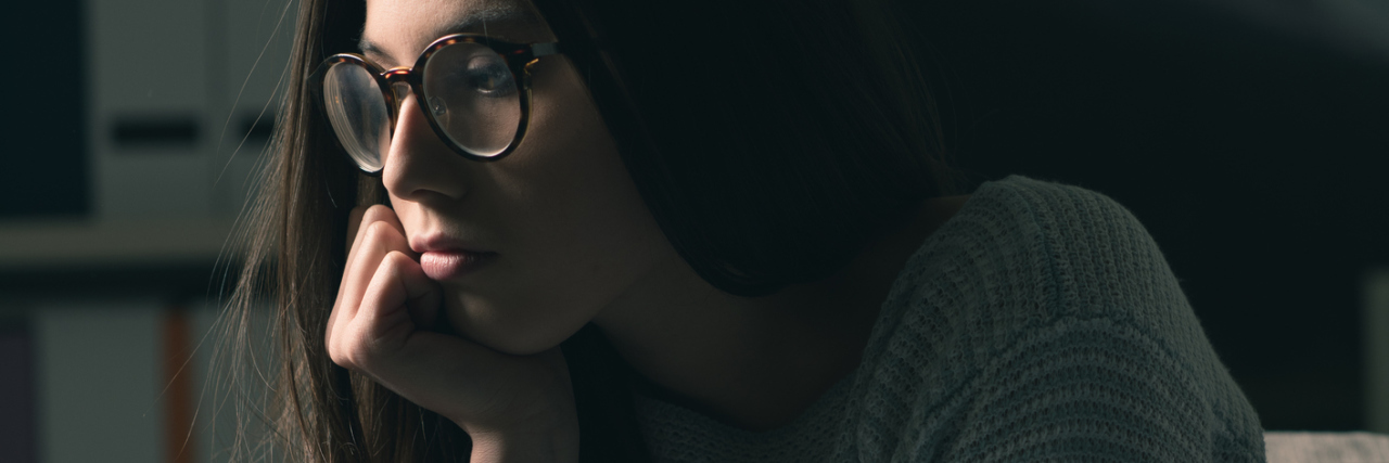 Sad young woman with glasses sitting on the couch at home